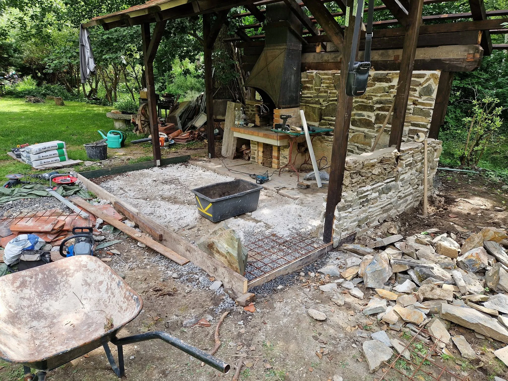 Bednění a armatura nové podlahy pod přístřeškem s krbem, okolo materiál a kolečko